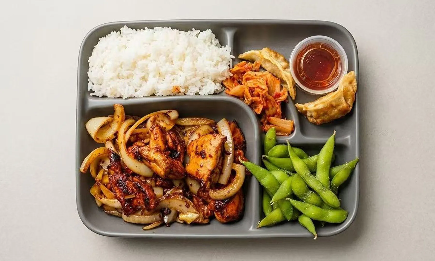 Bento box with teriyaki chicken, rice, kimchi, edamame, and gyoza