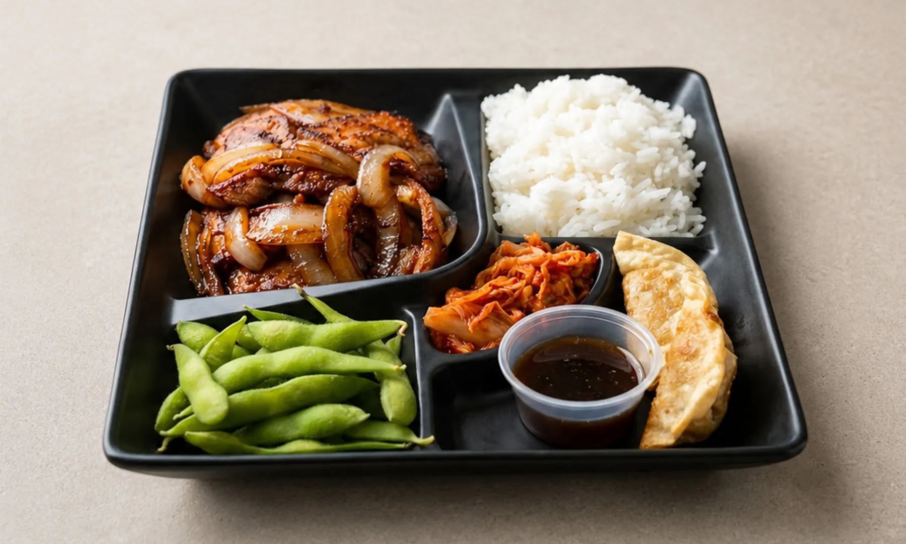 Bento box with teriyaki chicken, white rice, edamame, kimchi, and gyoza