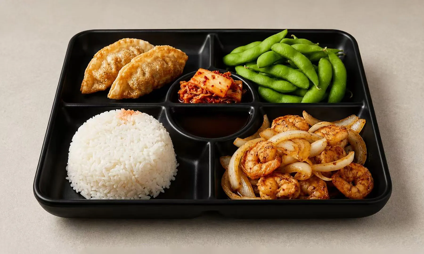 Bento box with teriyaki shrimp, rice ball, gyoza, kimchi, and edamame