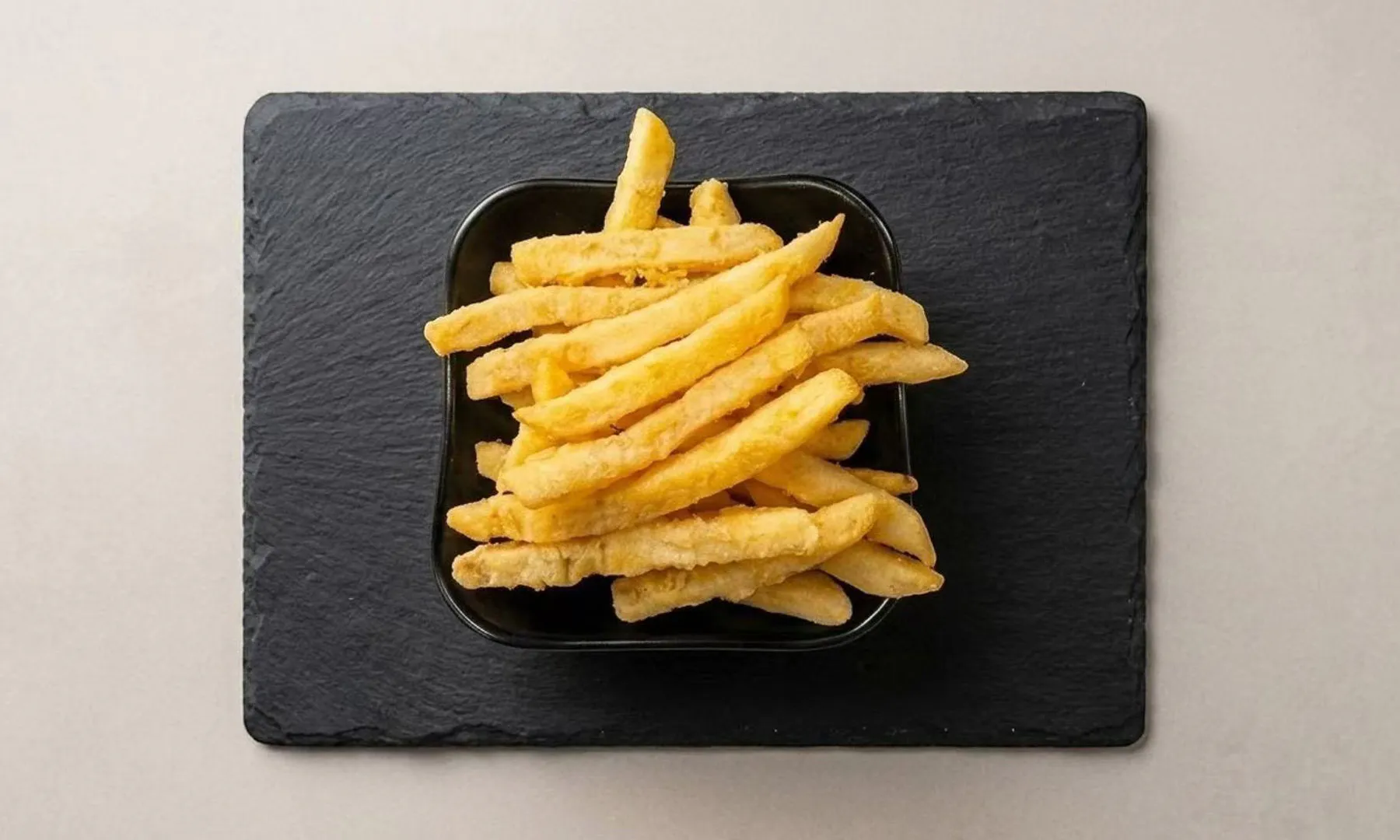 Golden crispy french fries in a bowl on a black slate board