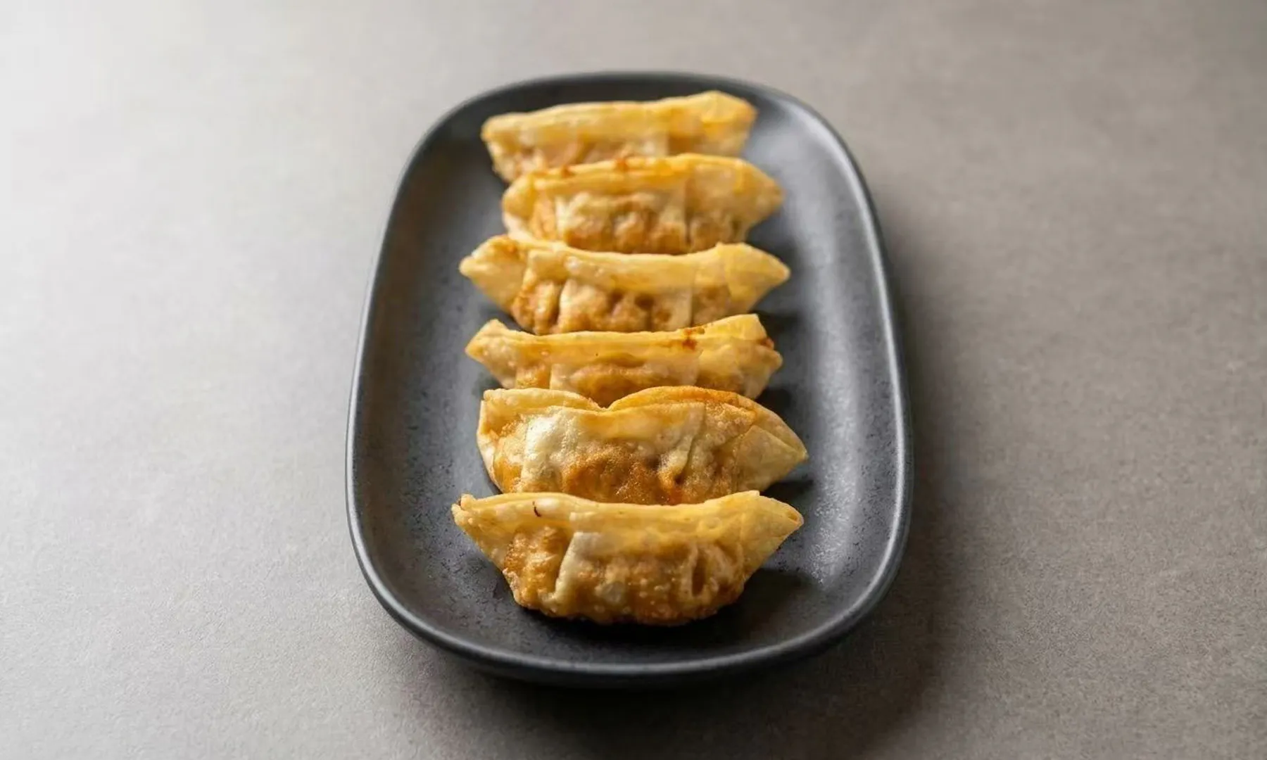 Six golden pan-fried gyoza dumplings lined up on a gray plate