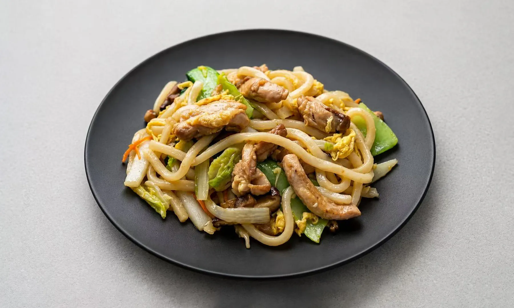 Stir-fried udon noodles with chicken, egg, and cabbage on a black plate