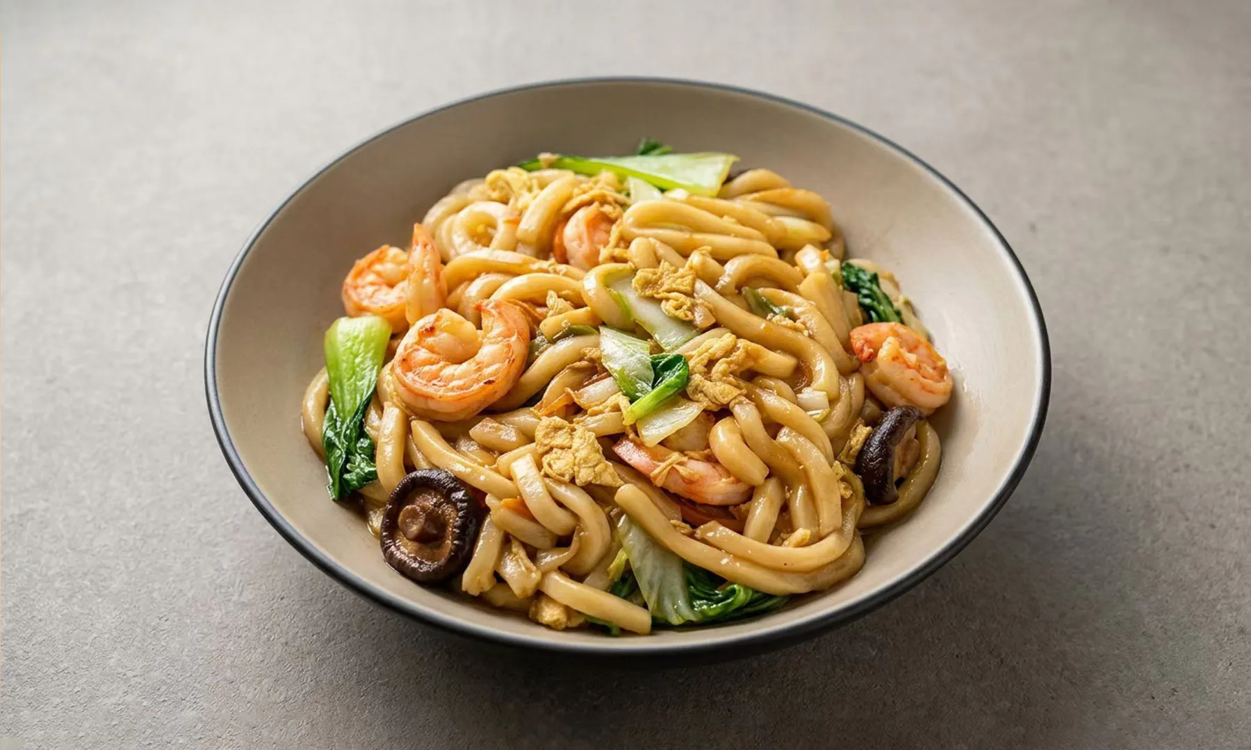 Stir-fried udon with shrimp, egg, mushrooms, and greens in a bowl