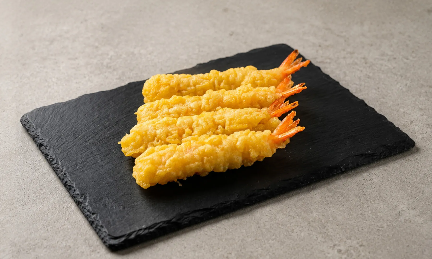 Three crispy shrimp tempura pieces on a black slate board